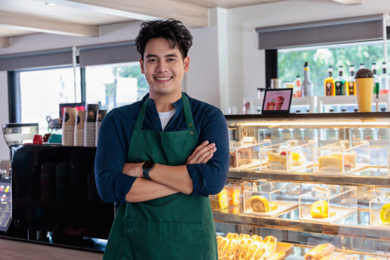 Small coffee shop owners standing with arms crossed looking at camera, smiling Asian male waiter or baristas welcoming customers in restaurant. small business concept