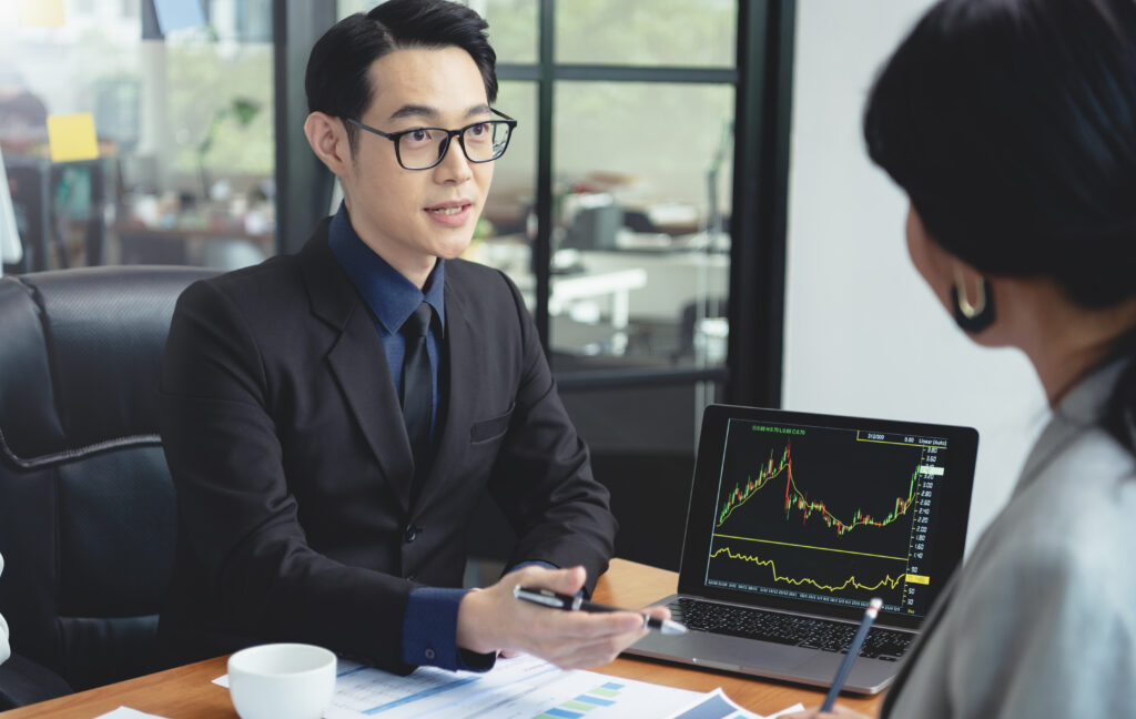 Group of Asian business people meeting about business plan and present and explain stock financial chart from laptop computer at office.