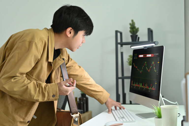 Side view of young businessman or trader standing in front of computer monitor with trading charts.